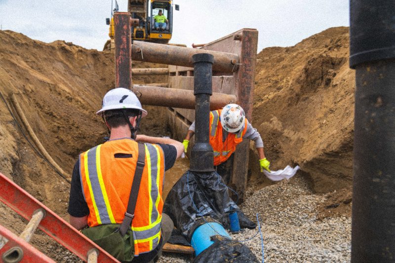 Workers in orange high-vis setting pipe in a shored trench