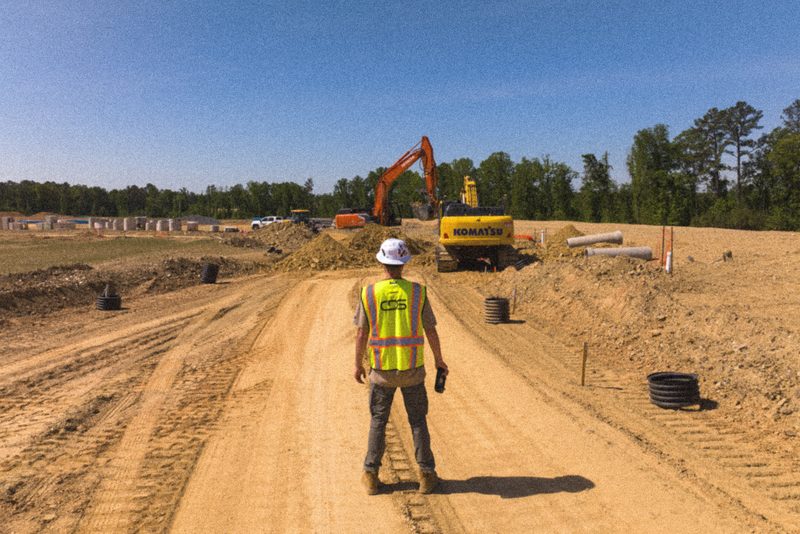 A lone crew member on a haul road, an excavator working the cut behind