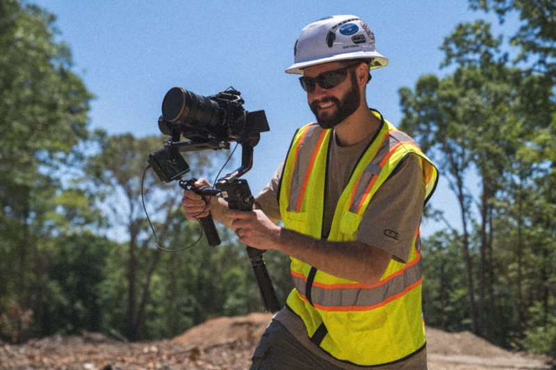 A CDS shooter in a hard hat running a gimbal rig on a cleared jobsite