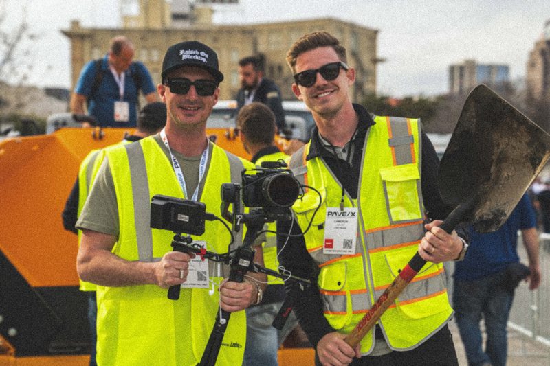 Two CDS shooters in high-vis on the PaveX demo lot, camera rig and a shovel between them
