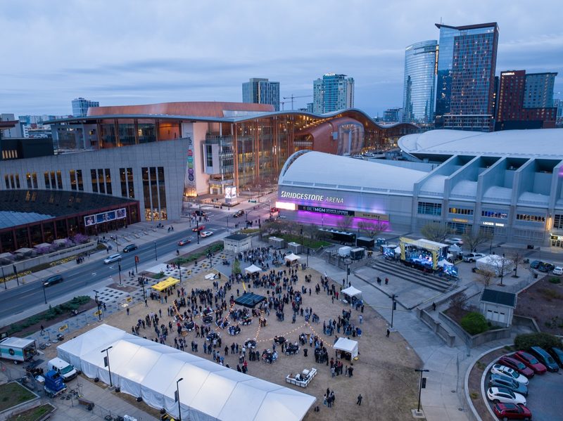 Dusk aerial over the arena plaza, event tents and the crowd filling the square