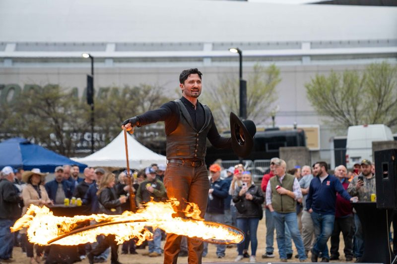 A fire performer working the crowd outdoors, flame arcing across the ground