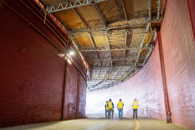 Three workers walking a lit corridor under the stands, red walls curving away