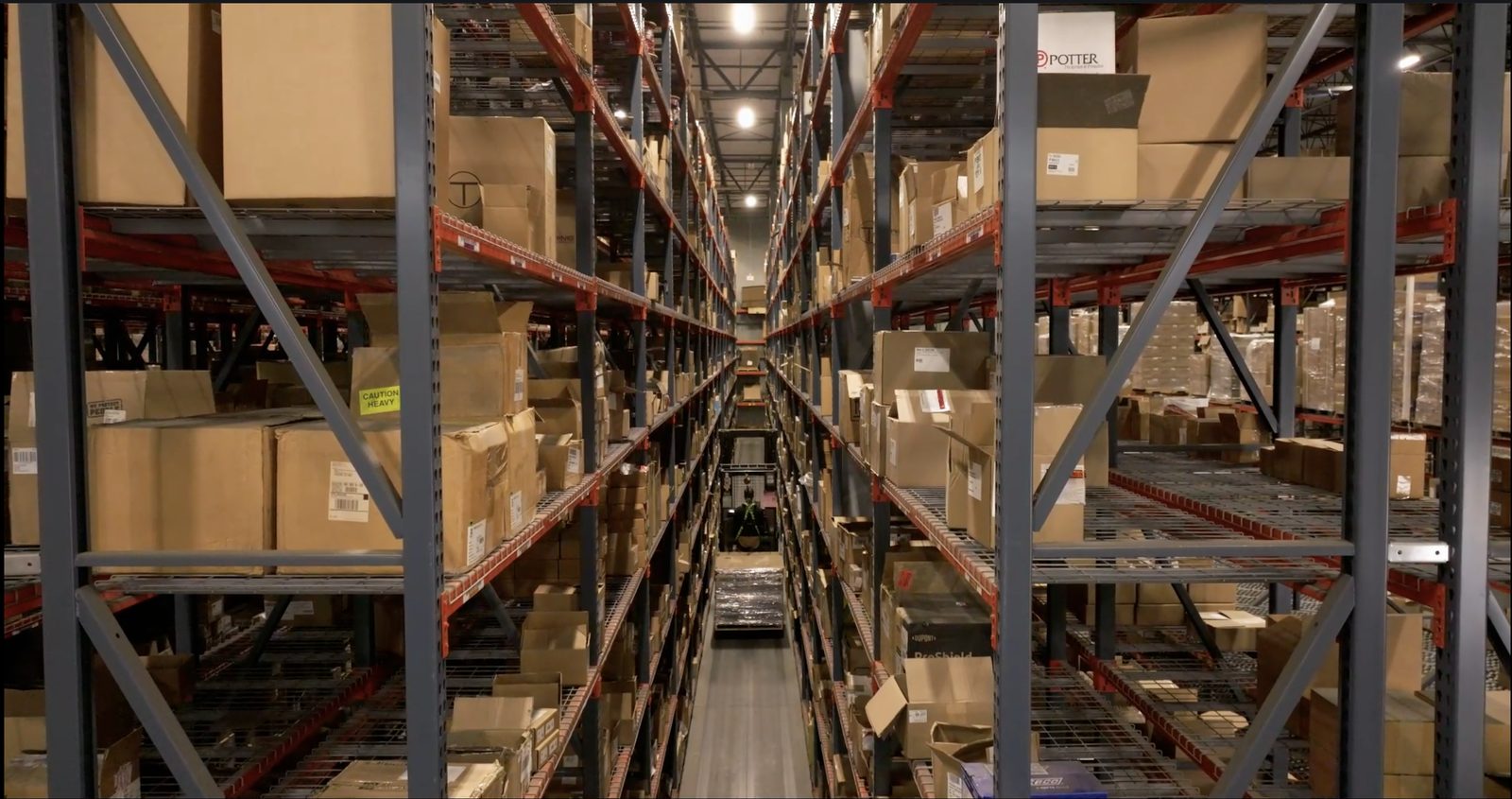 Looking down a warehouse aisle between tall pallet racking stacked with boxes on both sides