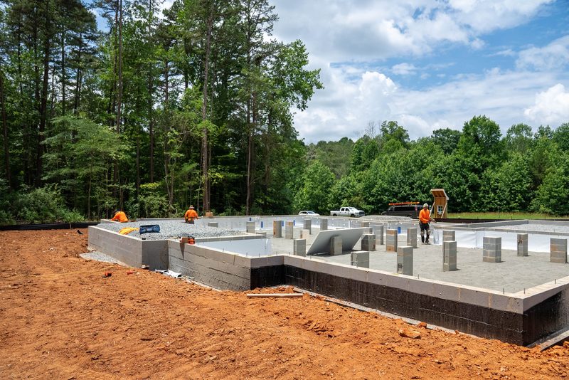 A block foundation wall going up on red clay, crew in orange working the deck