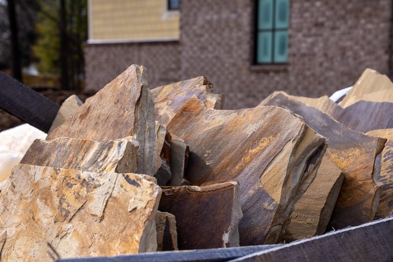 A stack of flagstone slabs waiting on the pallet, the house rising behind