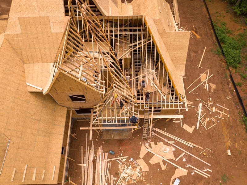 Aerial down onto a house at framing stage, sheathing on and lumber stacked below