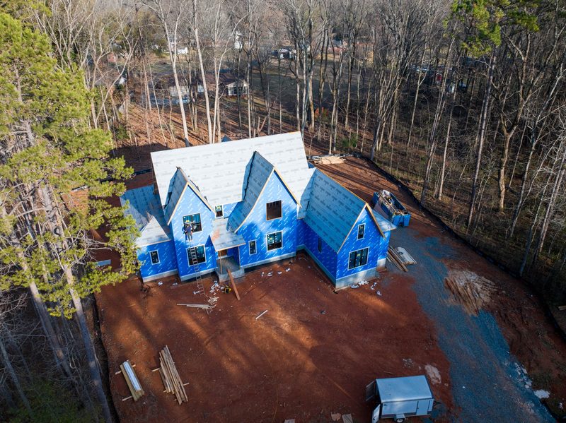 Aerial of the house in blue weather barrier, bare winter trees all around