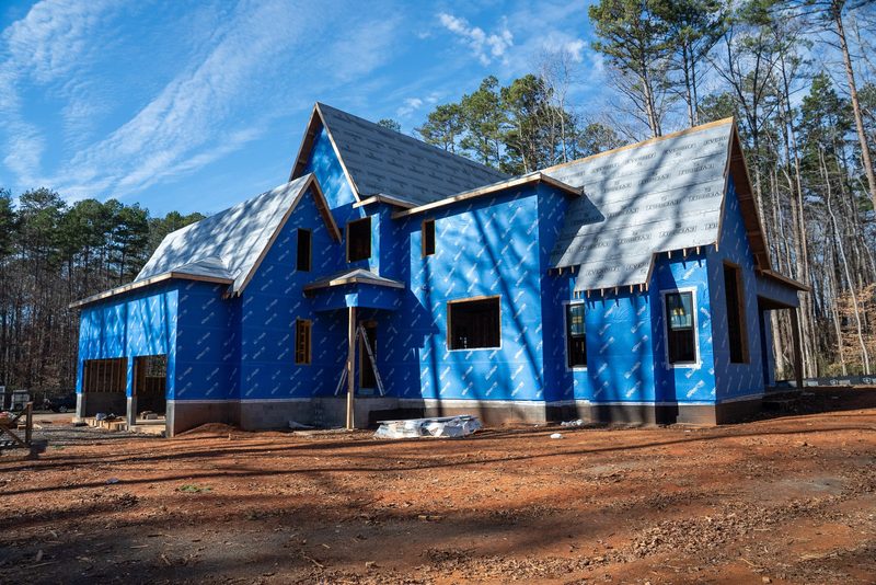 The house wrapped and roofed, sitting on bare red clay