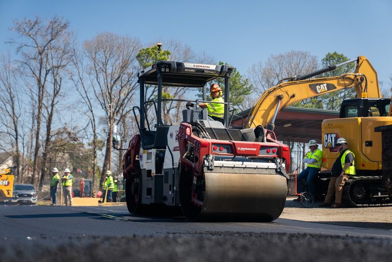 A Dynapac tandem roller sealing the fresh mat, excavator working behind