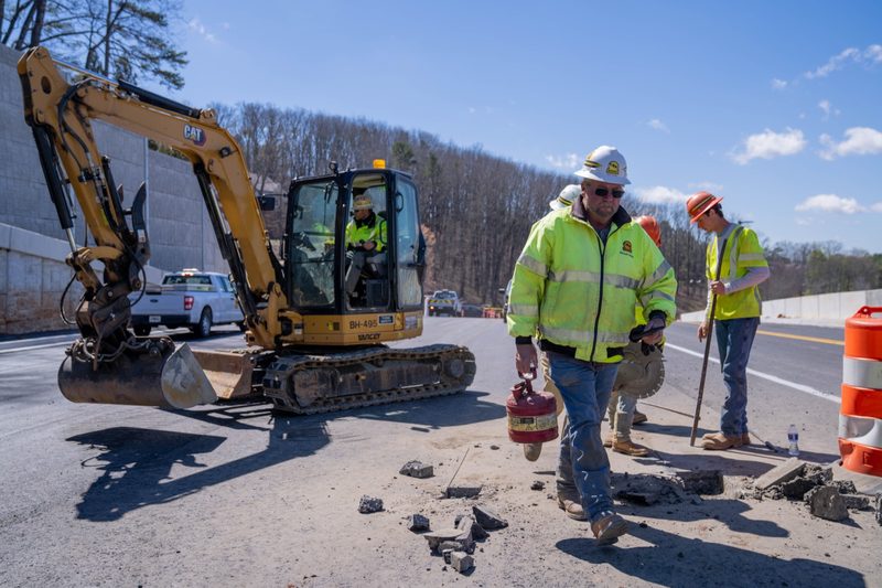 Crew walking the road past a mini excavator working the shoulder