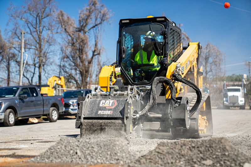 A CAT skid steer milling with a cold planer attachment, spoil curling off the drum