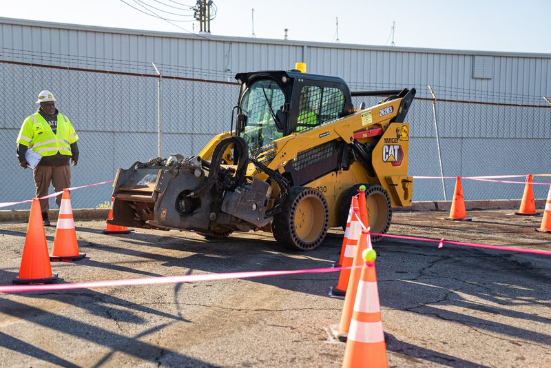A CAT skid steer picking its way through the cones
