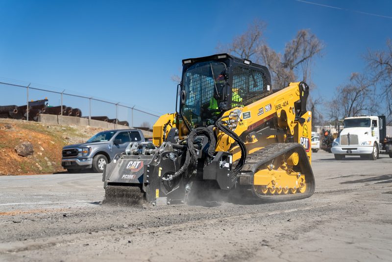 A CAT skid steer cutting asphalt with the cold planer, spoil kicking out behind