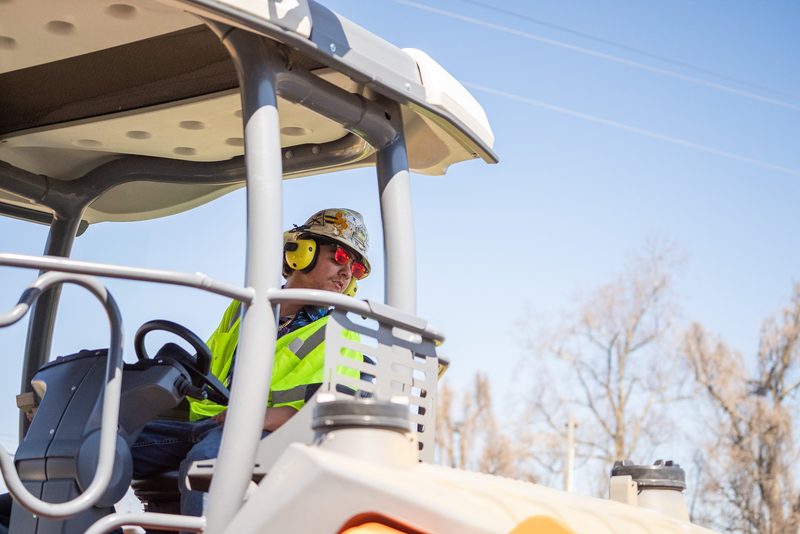 An operator in ear defenders at the controls, sun coming through the canopy