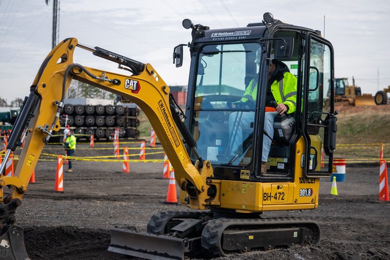 An operator threading a CAT mini excavator through the cone course