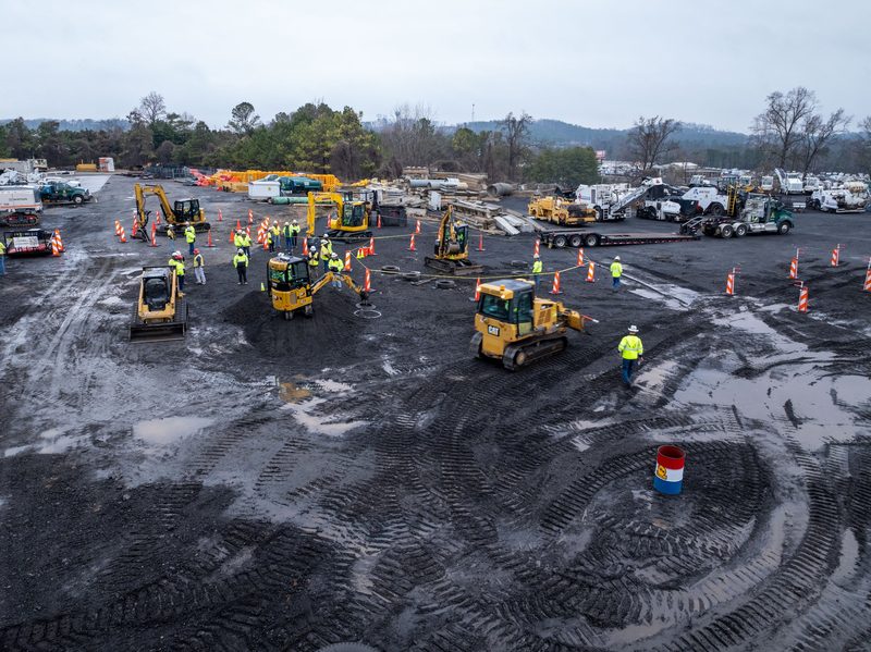 Aerial over the course, machines and spectators spread across the black dirt