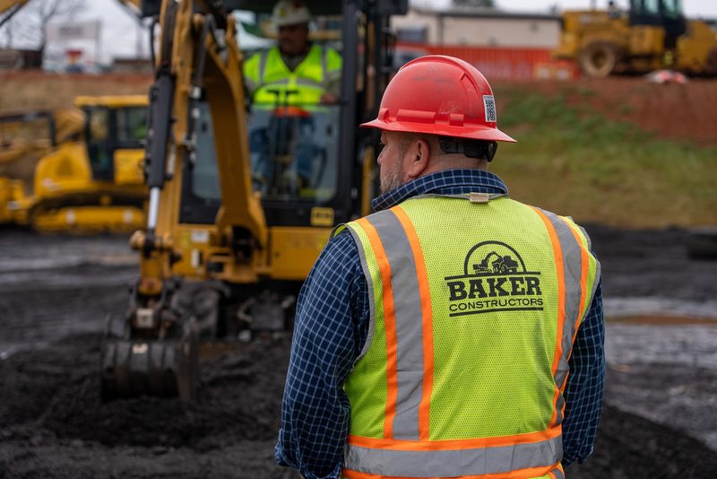 A spectator in high-vis and hard hat watching the excavator work the pile