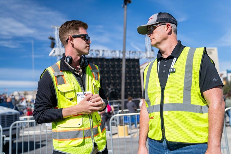 Two crew in high-vis talking at the demo area, barriers behind them
