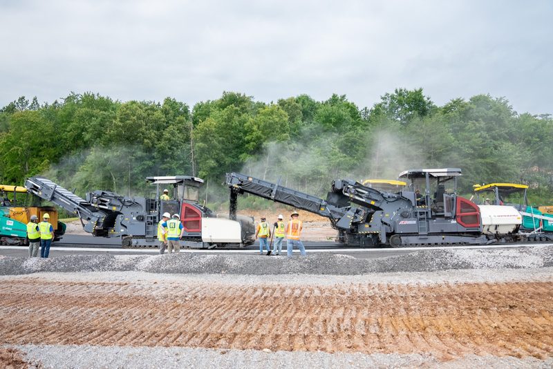 Wide on the paving train working a gravel base, crew in high-vis alongside