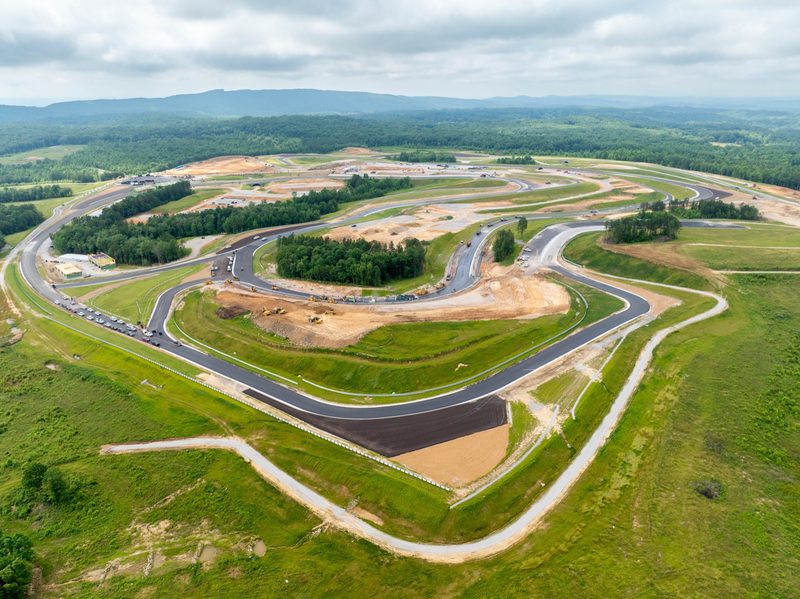 Aerial over a racing circuit under construction, fresh asphalt curving through green hills
