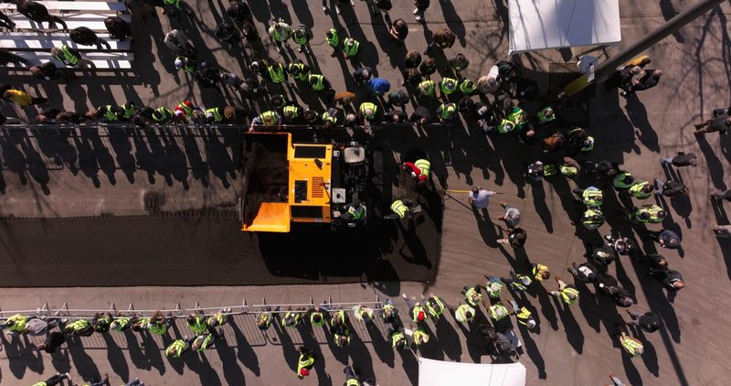 Straight down on the demo lot, long shadows off the crowd along the barrier