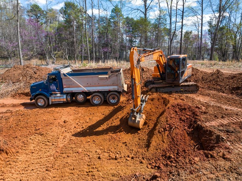 An excavator loading a dump truck on the red clay pad