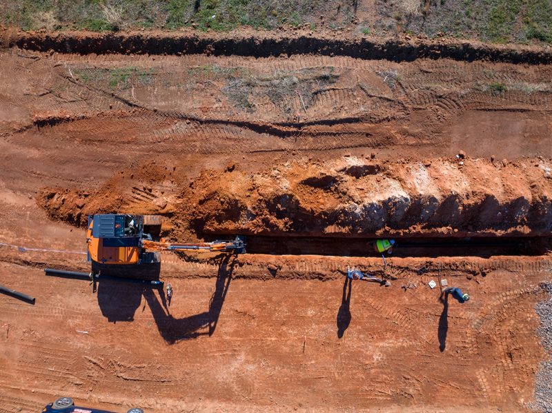 Aerial on the trench run, excavator working the backfill alongside