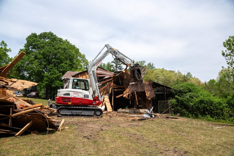 A Takeuchi excavator pulling down an old outbuilding