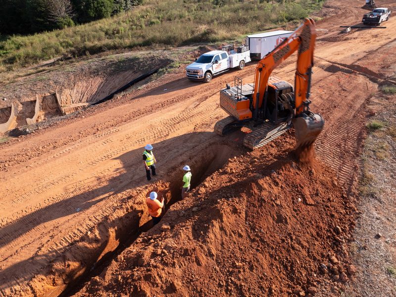 Aerial on the trench, two crew down in the cut with the excavator over them