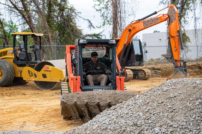 A track loader carrying gravel to the trench, roller and excavator behind