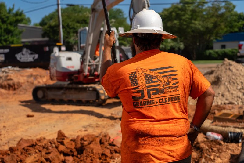 A foreman in a JP Grading & Clearing shirt watching the trench go in