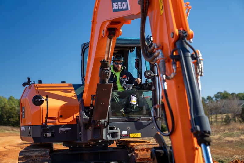 Low on a Develon excavator against open sky, the operator working the sticks