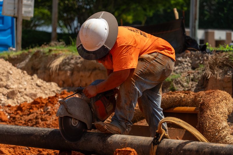 A worker cutting pipe over the trench, sparks off the saw