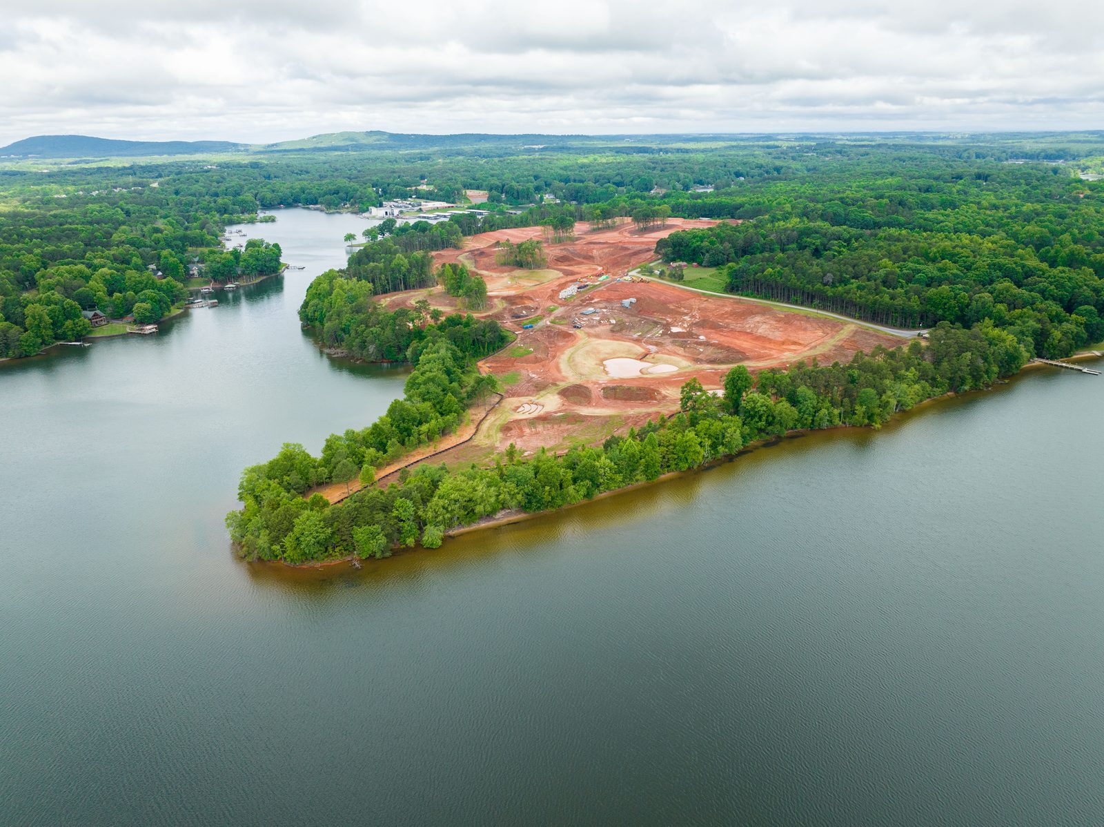 Aerial of a lakeside peninsula cleared and graded for development, water on both sides and trees along the shore