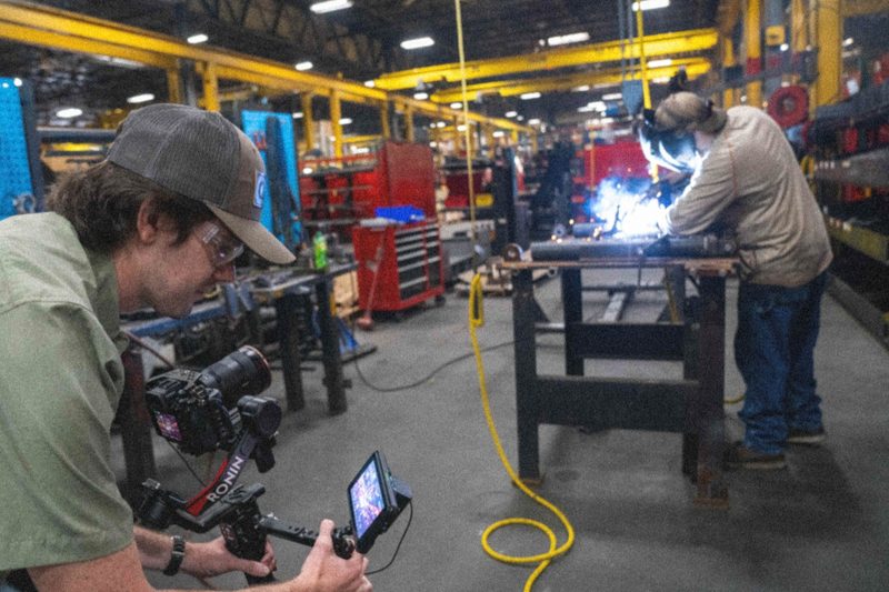 A shooter filming a welder at the bench on the factory floor