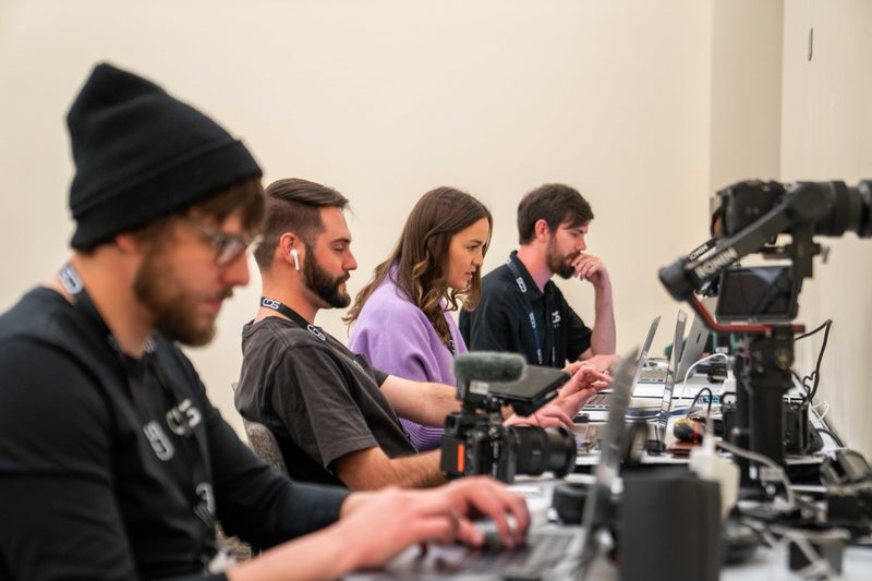 The crew heads-down at laptops on the edit bench, camera rig alongside