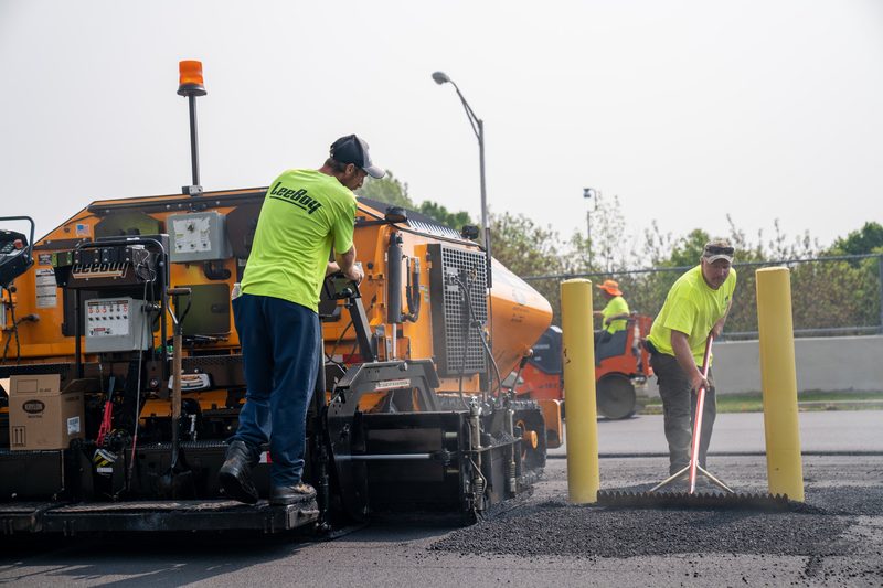 A screed hand raking the joint while the operator works the console above