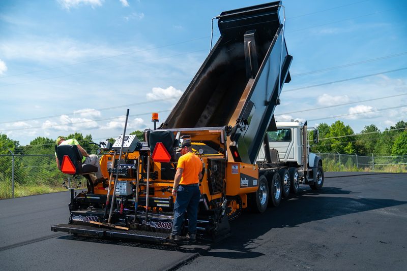 A dump truck feeding the paver on a clear day