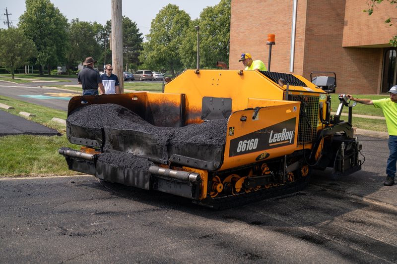 A LeeBoy 8616D paver with the hopper loaded, mid-pull on the street