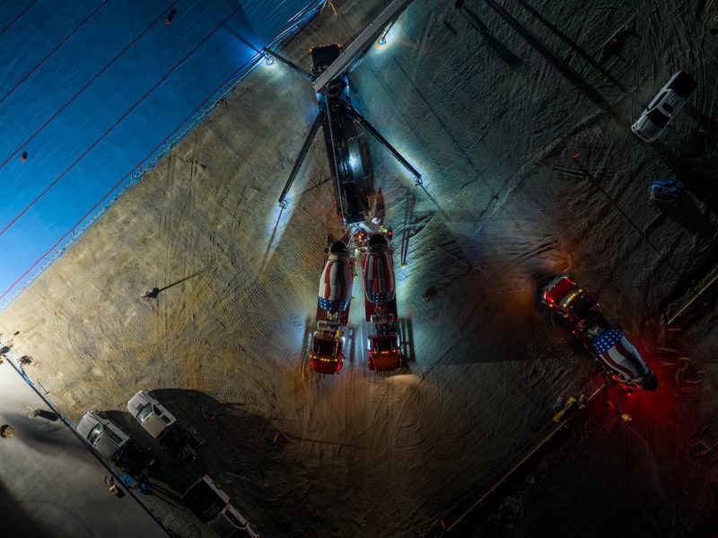 A canted night aerial down the length of the pour, work lights blazing