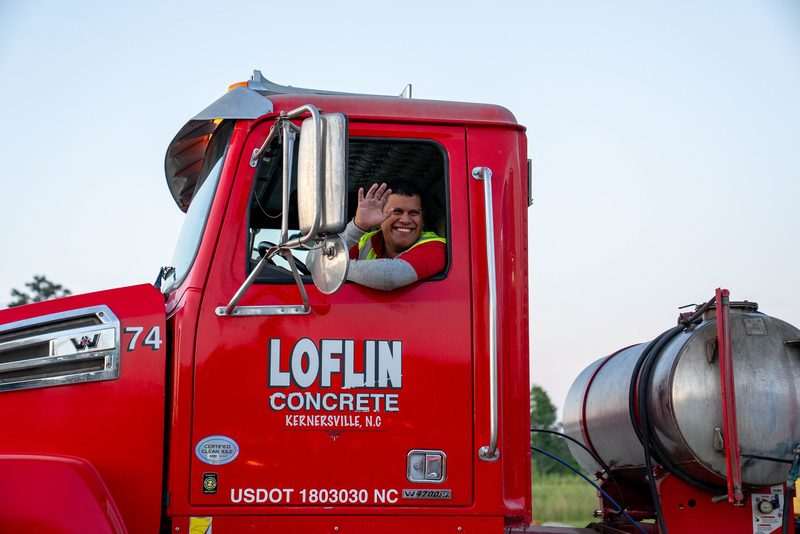 A driver waving down from the cab of a Loflin mixer