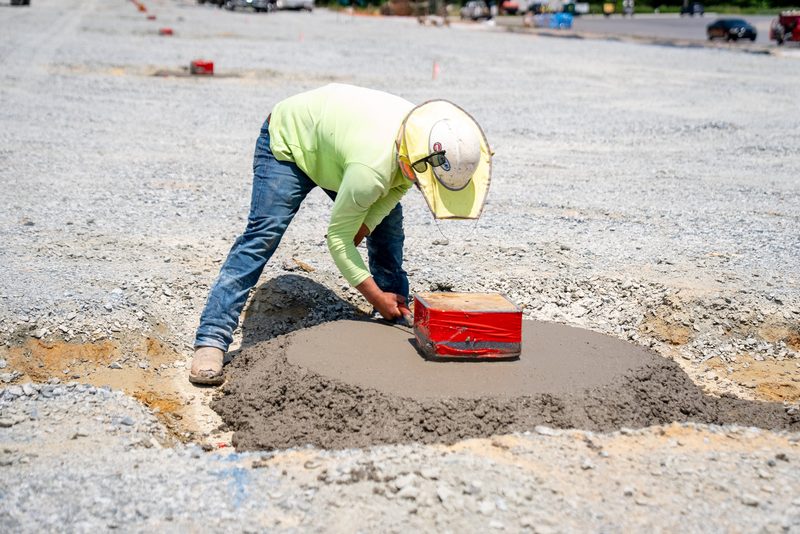 A worker placing concrete by bucket out on the gravel