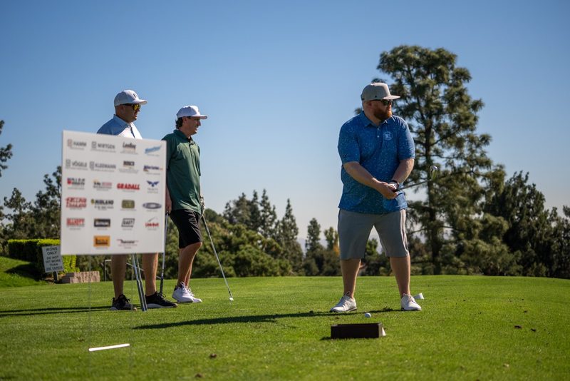 Players waiting at the tee beside the sponsor board