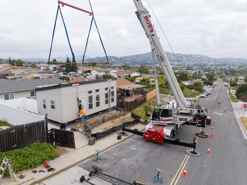 Aerial as the crane sets a unit into the yard beside the house