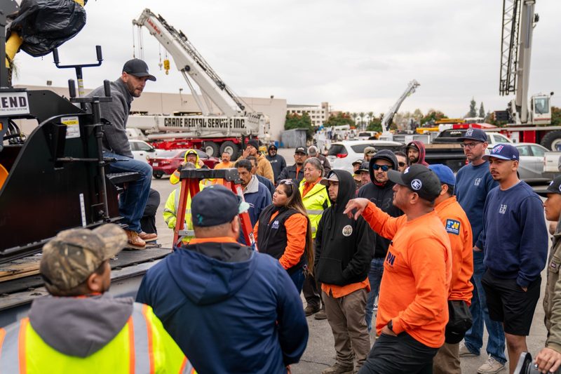 A crowd gathered for the outdoor demo, cranes standing behind