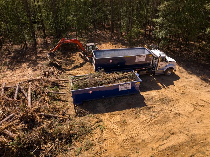 Aerial as the excavator loads brush into two containers at the treeline