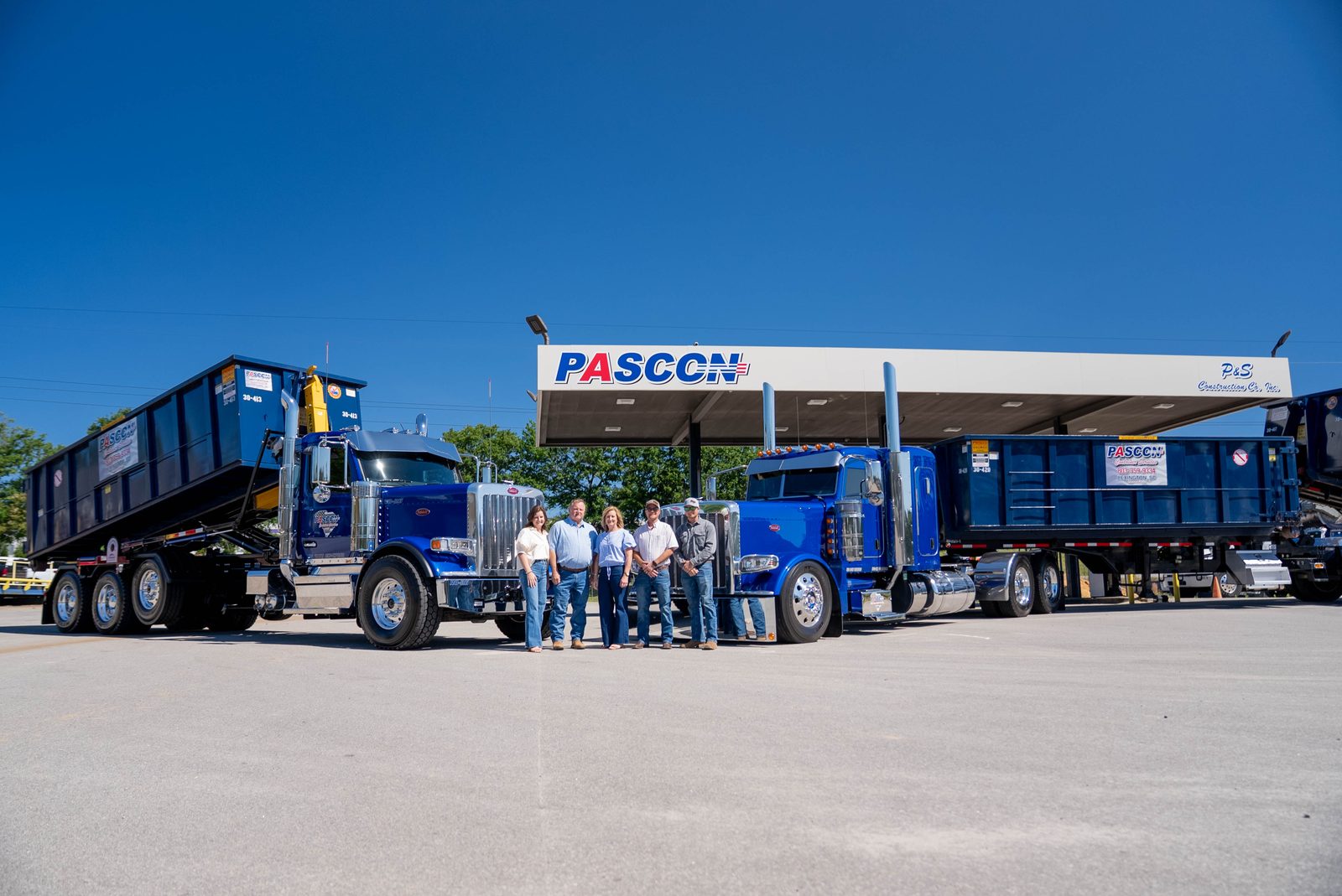 The Pascon crew standing together in front of a line of Pascon roll-off trucks and containers outside the building