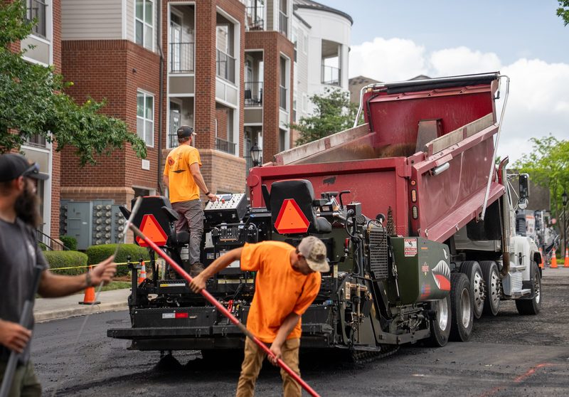 A truck feeding the paver at the building line, raker working the edge