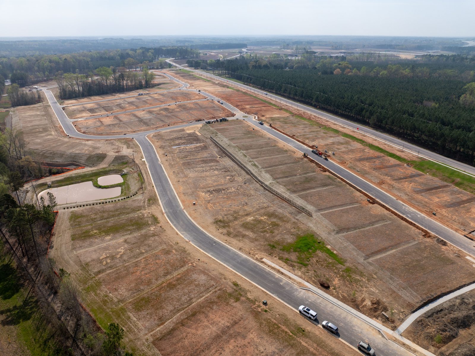 Aerial of a graded residential subdivision, new roads laid out through cleared lots with a pond at one edge